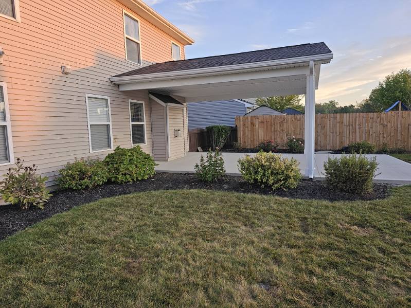 Covered concrete patio addition with white columns and shingled shed roof
