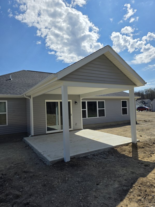 Covered concrete patio with tall gable roof and white posts on a new home