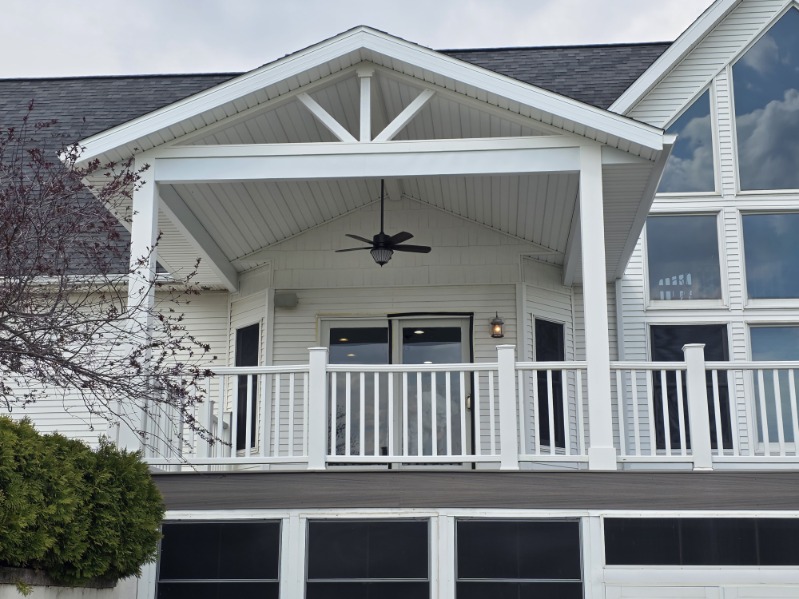 Elevated covered back porch with vaulted white ceiling, gable trusses, and ceiling fan overlooking a screened lower level