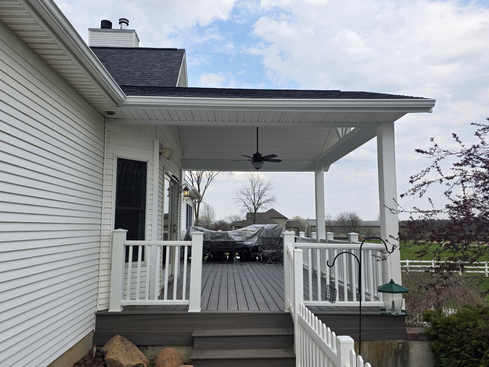 Covered gray composite deck addition with white columns and railing on a country home