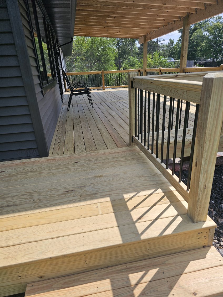New covered pressure treated wood deck with black balusters and step down landing