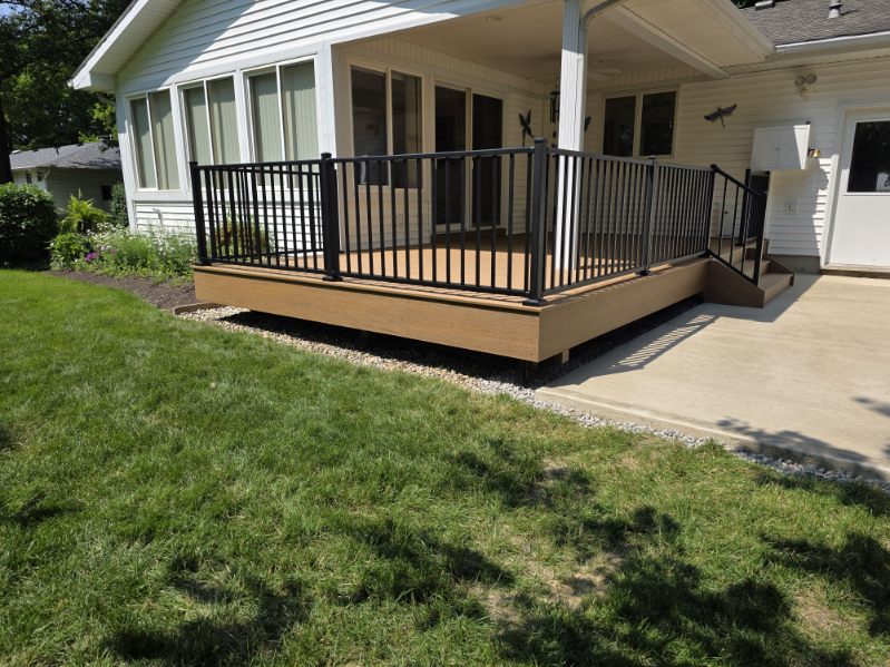 Composite deck with black aluminum railing next to a concrete patio in a landscaped yard