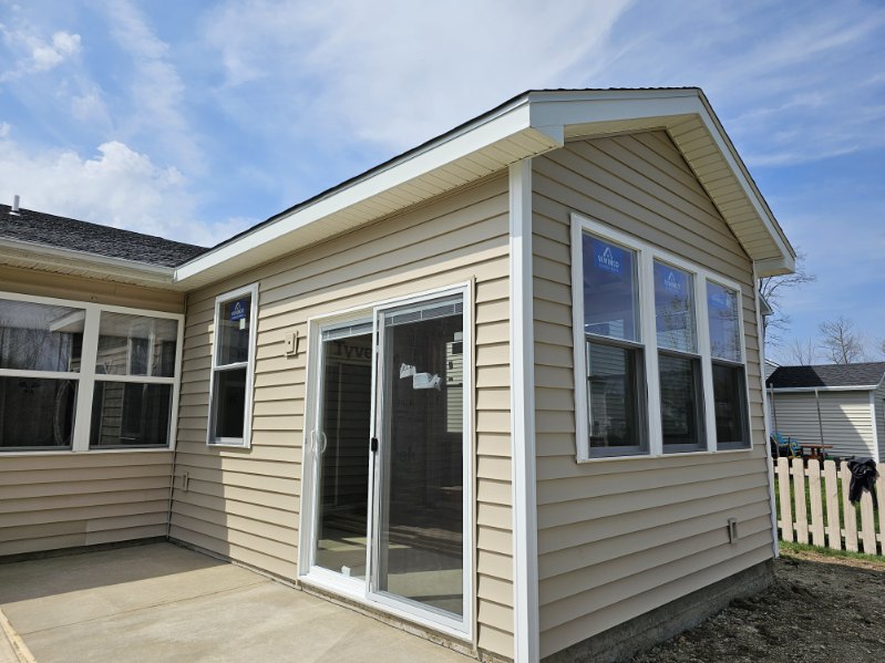 New sunroom addition with large windows, sliding door, and tan siding