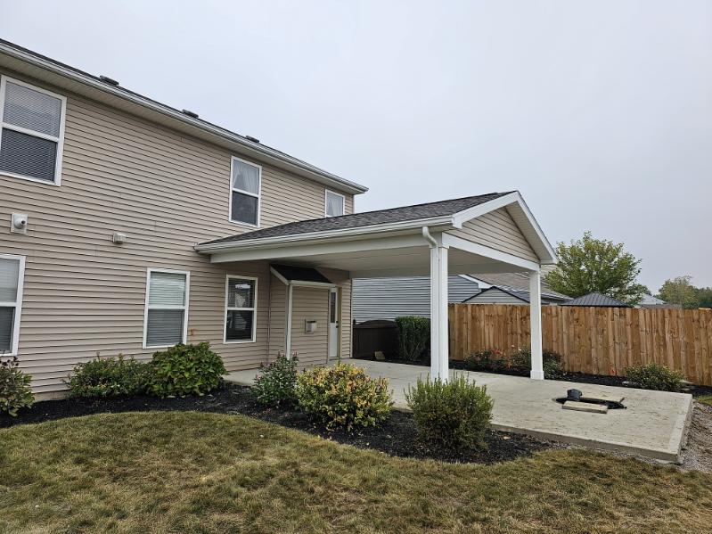 Covered concrete patio with white posts and gable roof attached to a two story home