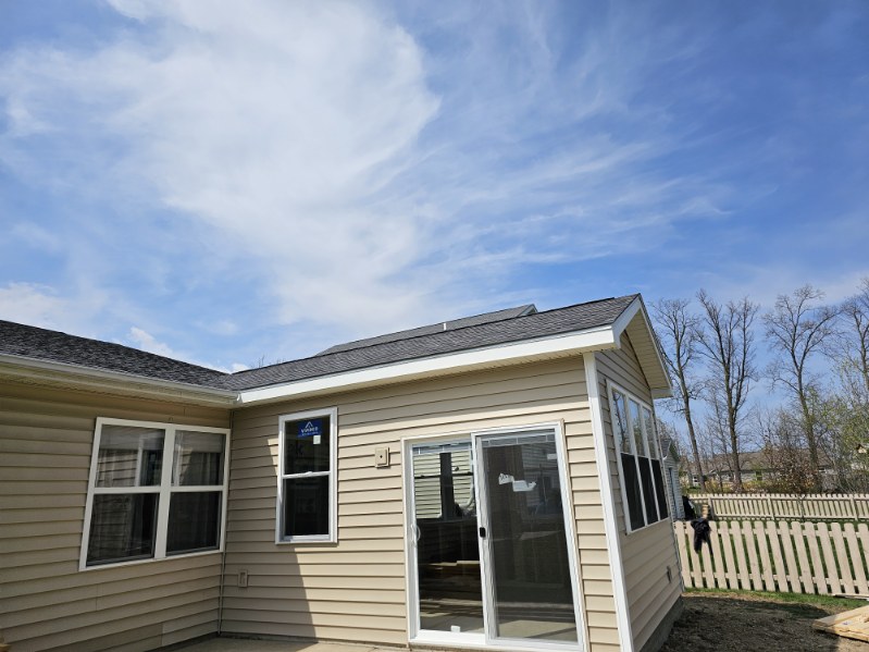Exterior view of a new room addition with sliding glass door and tan vinyl siding