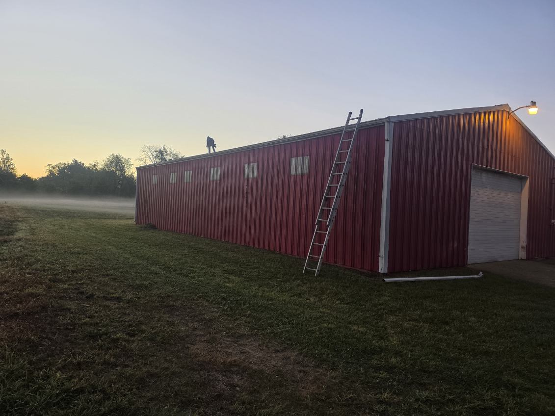 Red pole barn getting a new metal roof installed by T&J Construction at sunrise