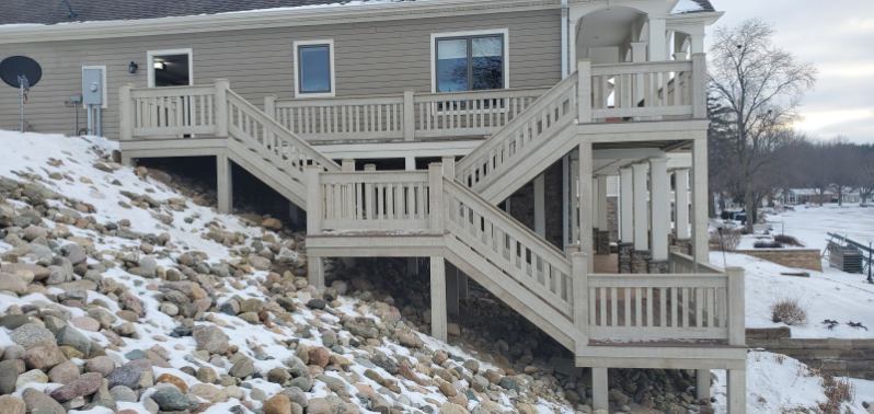 Large multi level painted lakeside deck with dual staircases over a rock embankment