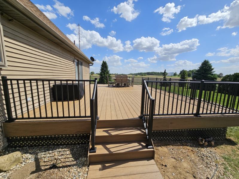 Two tone composite deck with staircase and black aluminum railing on a farmhouse