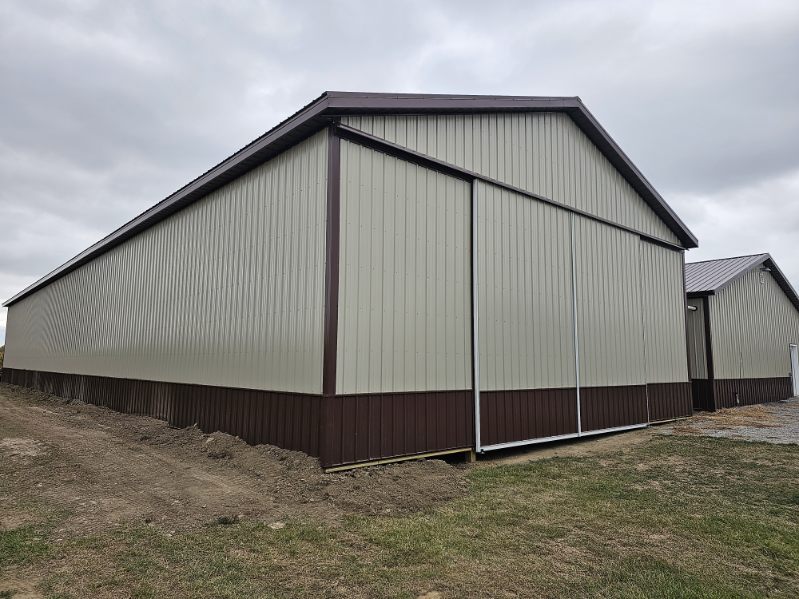 Tan pole barn with brown metal roof and wainscot on a rural Indiana property