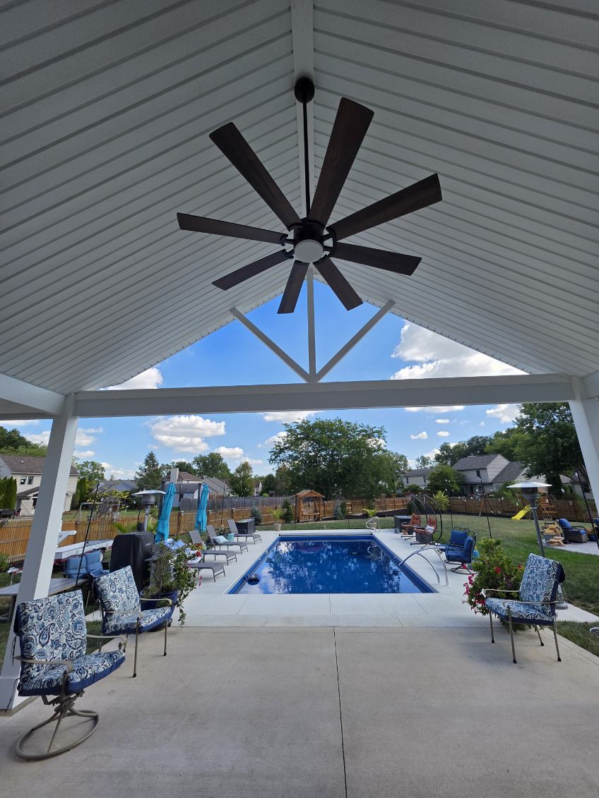 Covered poolside pavilion with vaulted white ceiling and large ceiling fan built beside an in ground pool